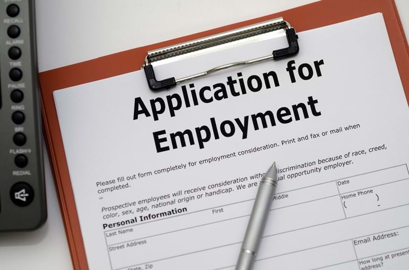 An application for employment form on a clipboard with a pen.