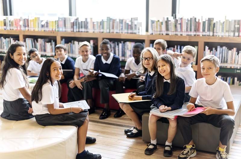 A group of school students sitting down on chairs in a library.